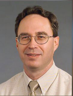 A man with glasses and dark hair smiling at the camera.