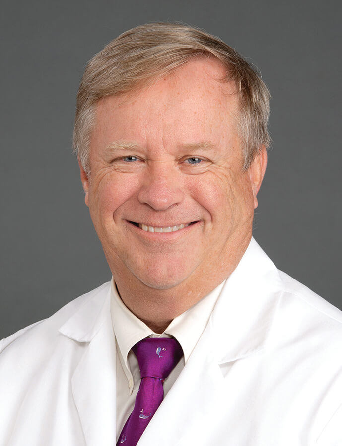 A man with blonde hair wearing a lab coat smiling at the camera.