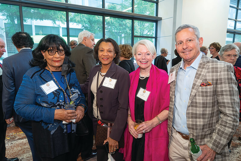 Three women and one man standing side-by-side smiling at the camera.