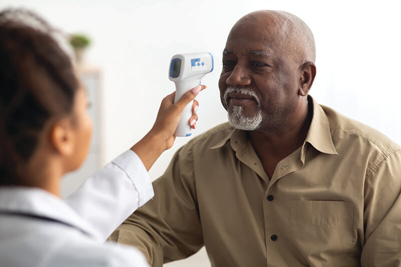 An older man getting his temperature taken with a forehead thermometer.