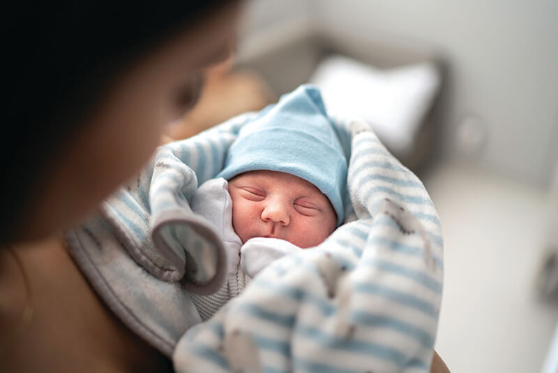 A newborn wrapped in a blanket wearing a hat.