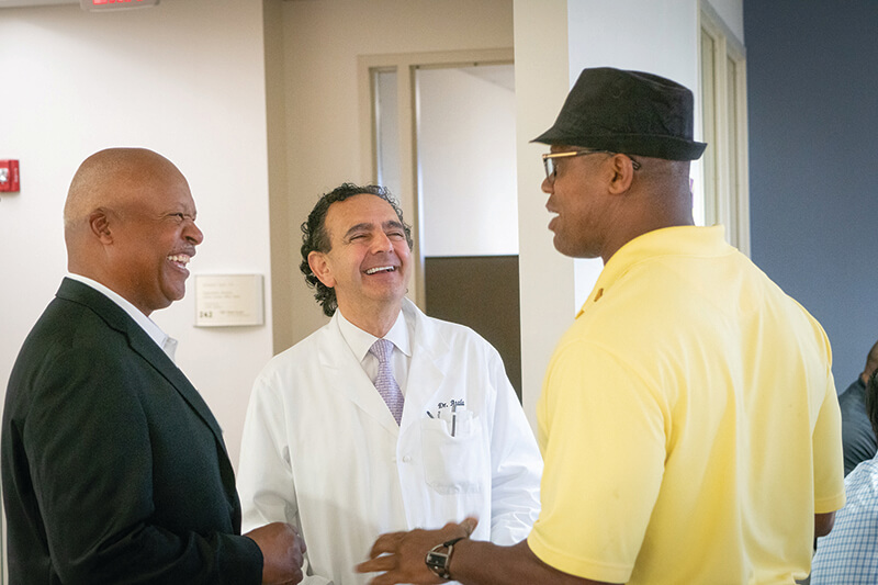 Three men standing in a group talking and laughing.