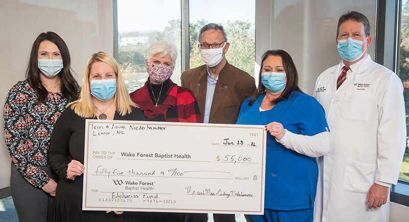 A group of men and women wearing face masks and holding an oversized check stand in front of large windows