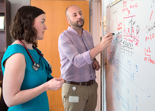 A man and a woman stand at a whiteboard and look at the numbers