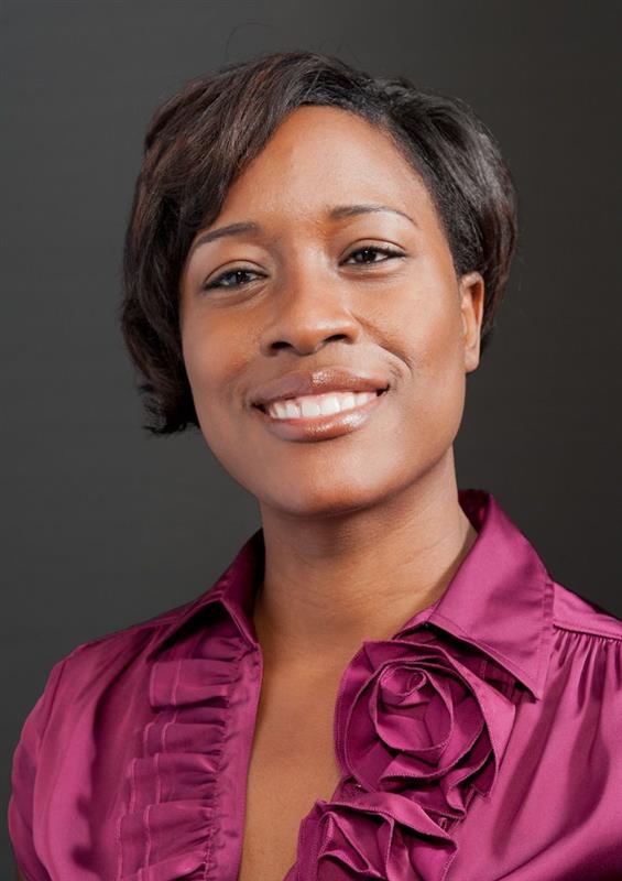 An African American woman wearing a plum-colored blouse with a ruffled collar smiles at the camera