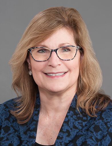 A woman with blond hair wearing glasses smiling at the camera.