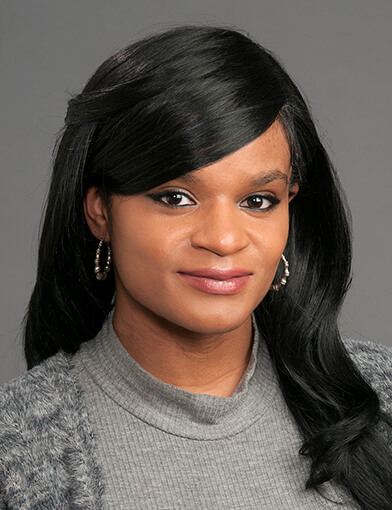 A woman with long dark hair, wearing a gray shirt and looking at the camera.