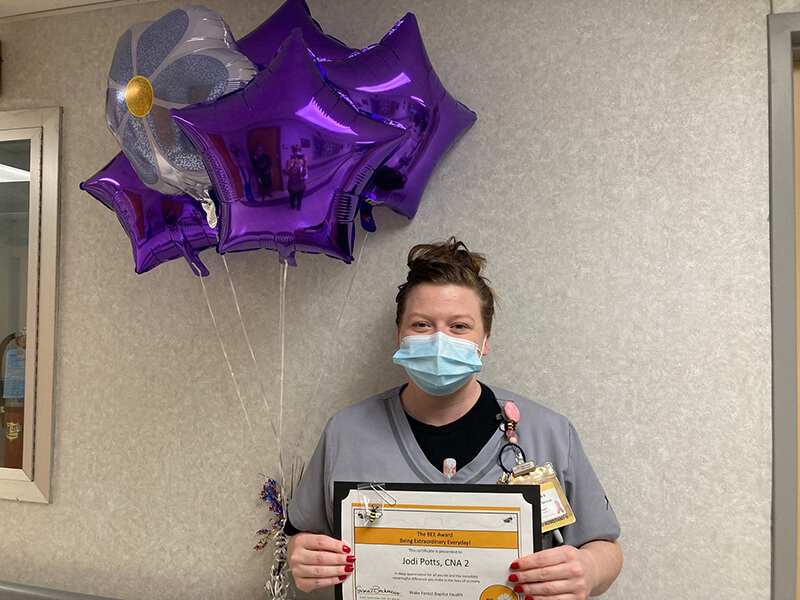 A young woman holding an award and purple balloons.