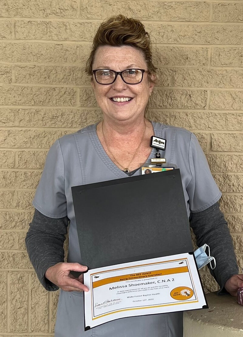 A woman holding an award certificate smiling at the camera.