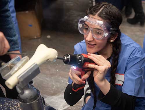 A high school student practices drilling into a bone model to place an ACL graft.