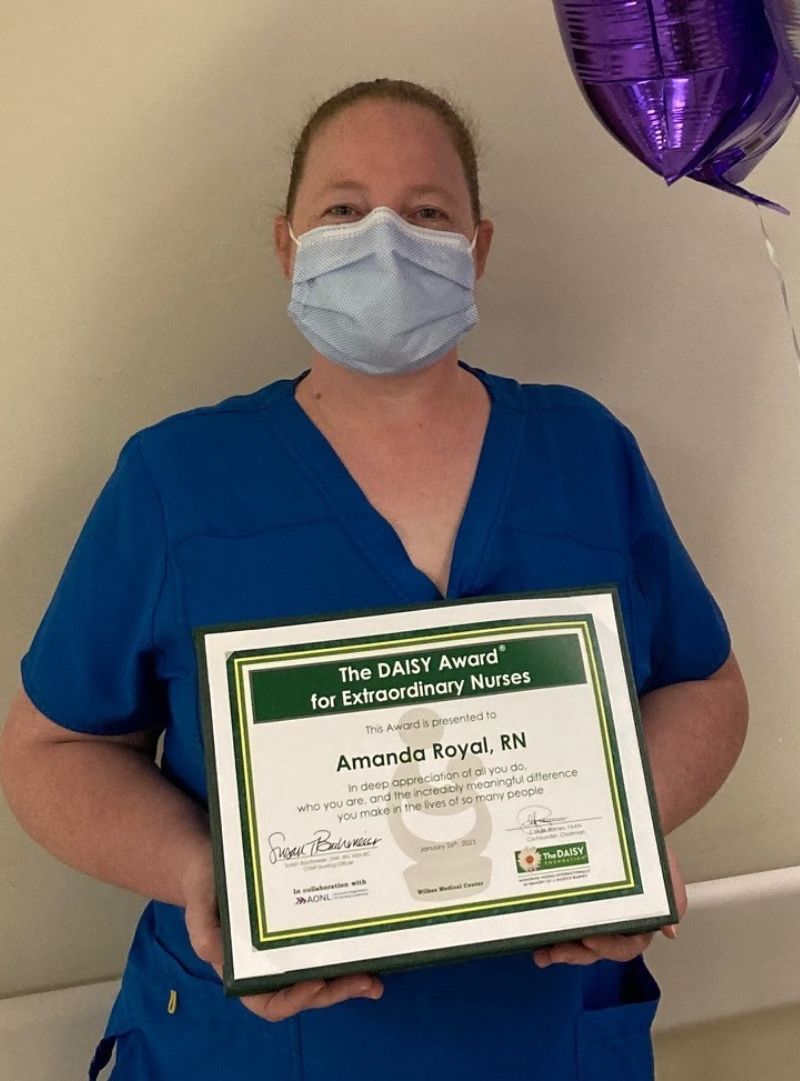 Amanda Royal, wearing medical scrubs holding an award and wearing a blue face mask.