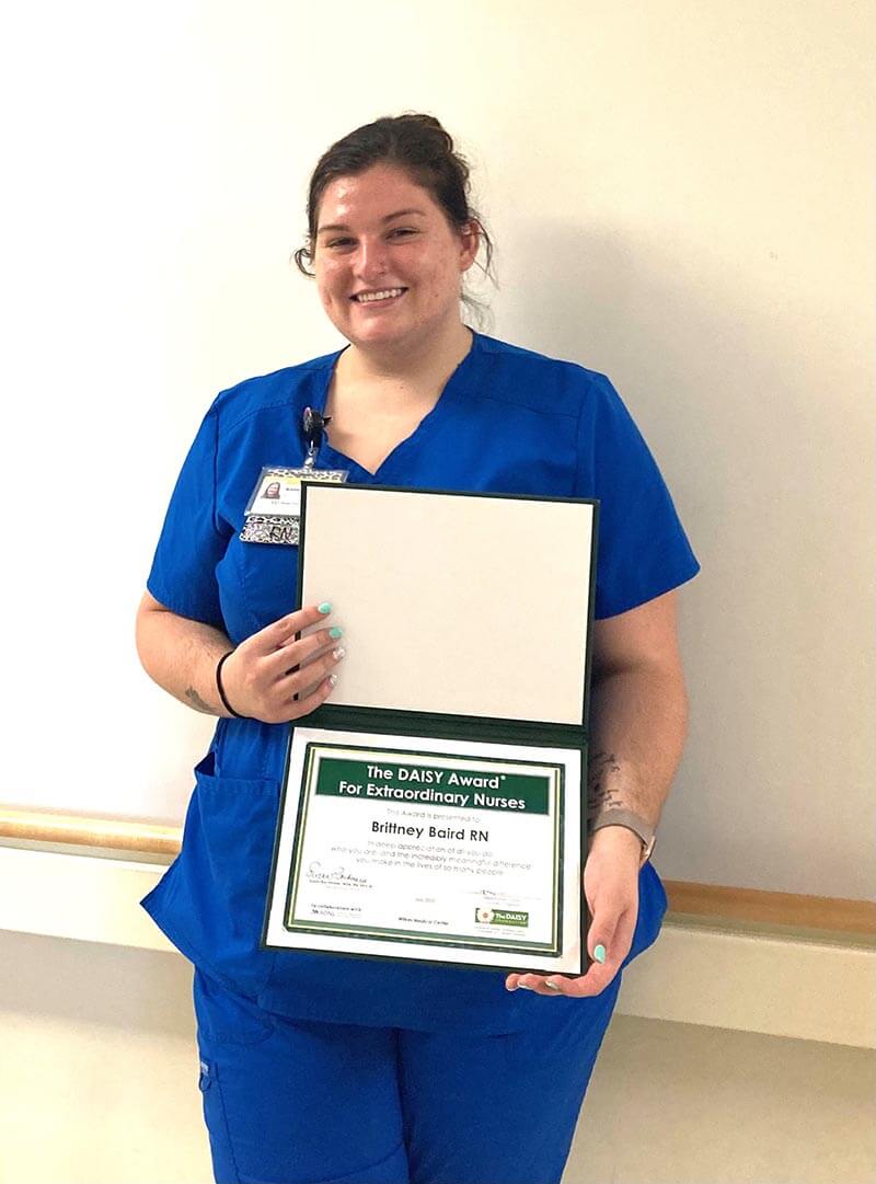 A woman wearing medical scrubs holding an award and smiling at the camera.