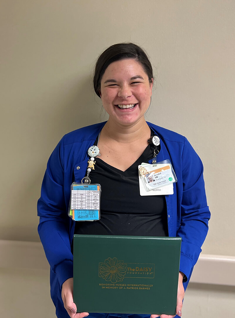 Kendall Letendre, wearing medical scrubs holding an award and smiling