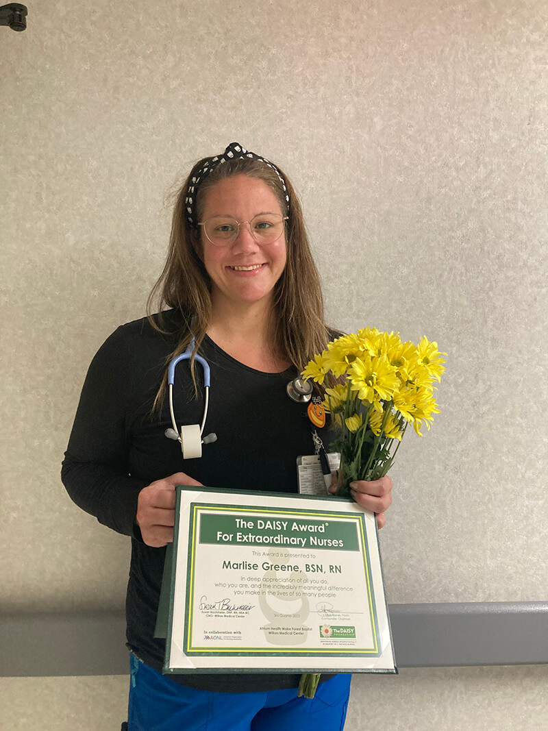 A woman holding a certificate and flowers and smiling at the camera.