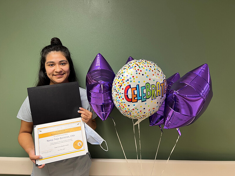 A young woman standing next to balloons, smiling at the camera and holding up a certificate.