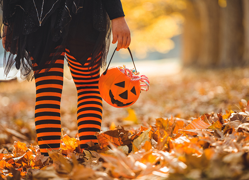 Girl trick-or-treating in striped leggings while carrying a pumpkin. 