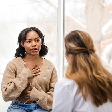 A young woman holding a hand on her chest while talking to a medical provider.