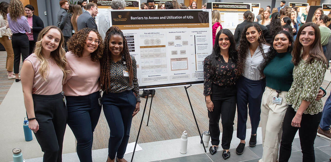 A group of women standing next to a poster at the 2024 PA Grad Symposium.