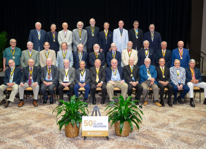 Photo of men sitting and standing, smiling wearing medals at Alumni Weekend 2023 at Wake Forest University School of Medicine.