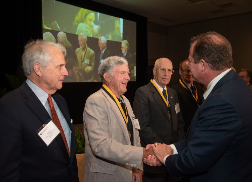 Two men wearing suits while shaking hands and smiling at Alumni Weekend 2023 at Wake Forest University School of Medicine.
