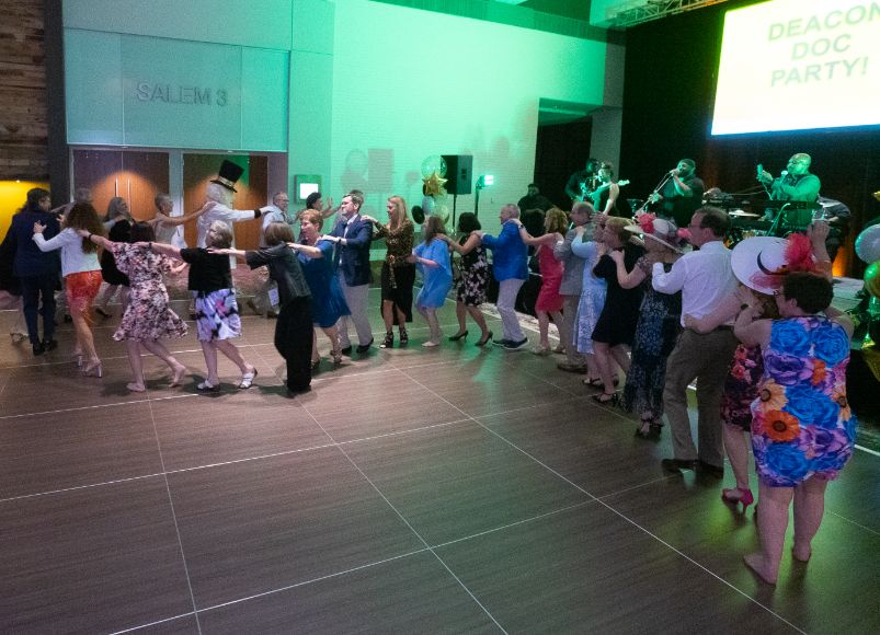 Group of well dressed people dancing inside an auditorium at Alumni Weekend 2023 at Wake Forest University School of Medicine.