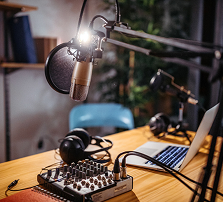 Laptop and microphone sit on a desk with a lamp