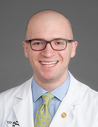 Bald white man wearing glasses and a white coat