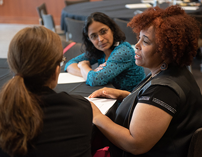 Three women sit at a round table and are involved in a discussion