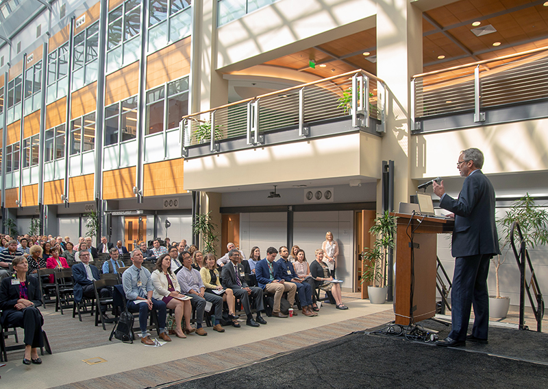 Mark Hall stands at podium and speaks to crowd in the atrium of Biotech Place