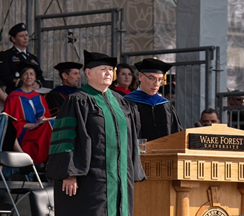 Sandra Ouellette wears black robe and green stole as she stands at a podium while accepting an honorary degree from Wake Forest University