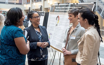 Group of women stand at a research poster and talk in the atrium of Biotech Place