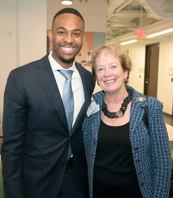 A tall African American man wearing a suit smiles and stands next to a Caucasian woman with reddish hair and wearing a suit