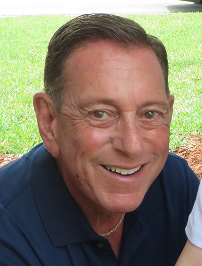 Close-up face shot of main with dark hair and eyes, smiling at camera