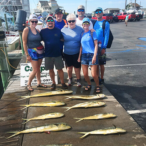A group of people standing in front of fish they caught on a fishing trip.