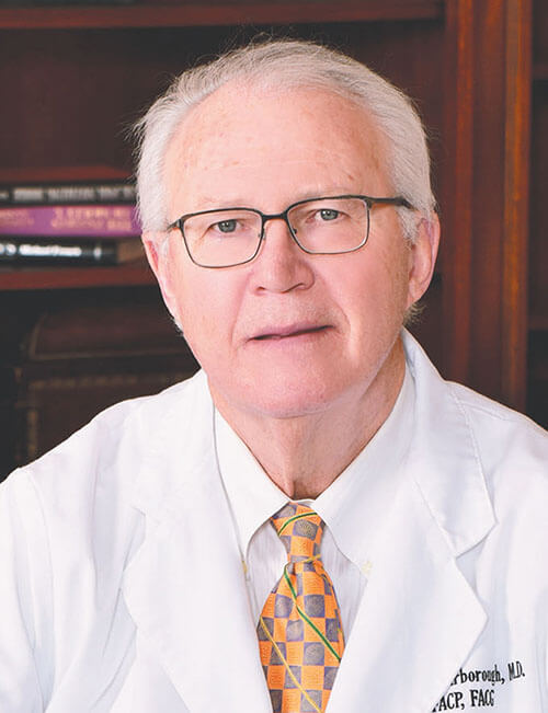 An older man wearing a white coat and looking at the camera.