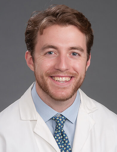 A young man in a lab coat smiling at the camera.