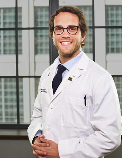 A young man wearing a lab coat smiling at the camera.