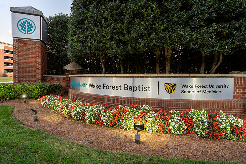 A metal sign over brick that read Atrium Health Wake Forest Baptist and Wake Forest University School of Medicine.