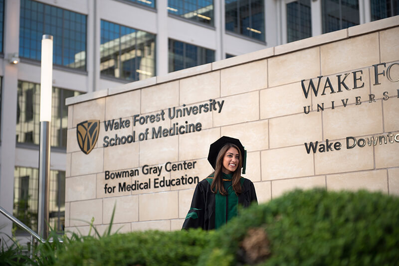 A young graduate walking in front of signage for Wake Forest University School of Medicine.