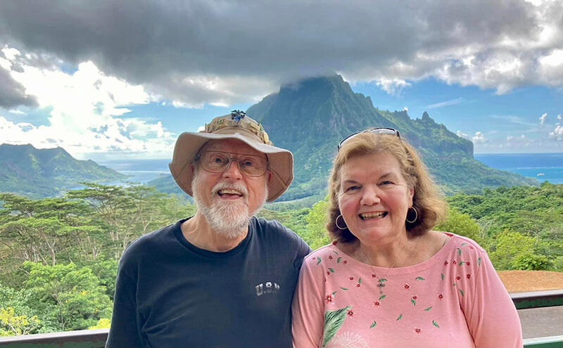 An older couple standing at the base of a mountain smiling at the camera.