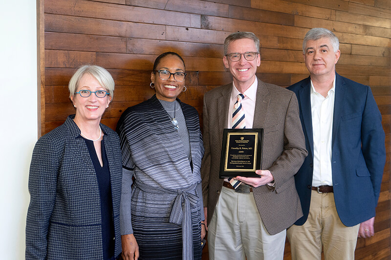 Four people, one holding an award, standing side-by-side smiling at the camera.