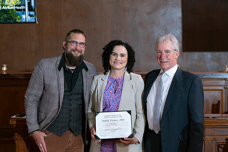 Three people, one holding an award, standing side-by-side smiling at the camera.