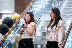 Two women standing on stage speaking to a crowd.