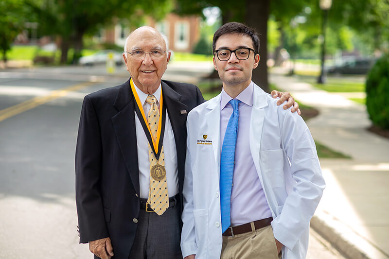 An older man standing next to a younger man wearing a lab coat.