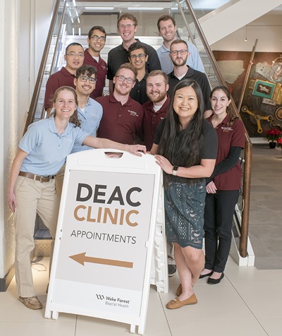 School of Medicine students stand on stairs above a sign for the DEAC Clinic