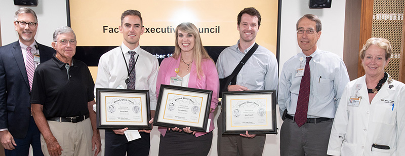 A line of faculty and three students stand in a line, and the students each hold a certificate