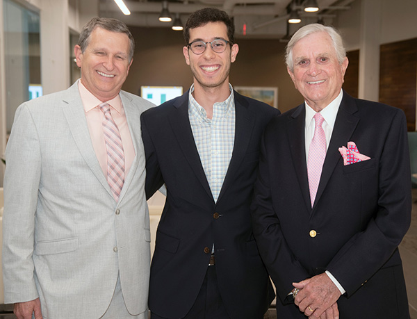 Three men, ranging in age, stand together and smile for the camera