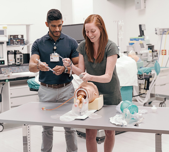 A young woman and young man laugh as they attempt to intubate a mannikin