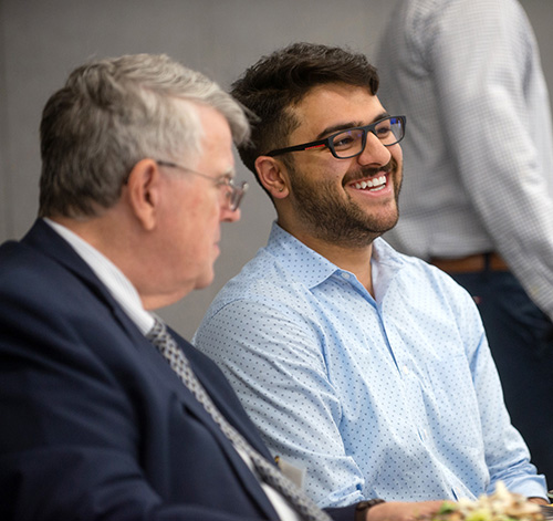 An older man and a younger man talk and laugh as they sit together