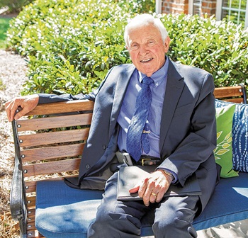 An older Caucasian man sits on a bench outdoors
